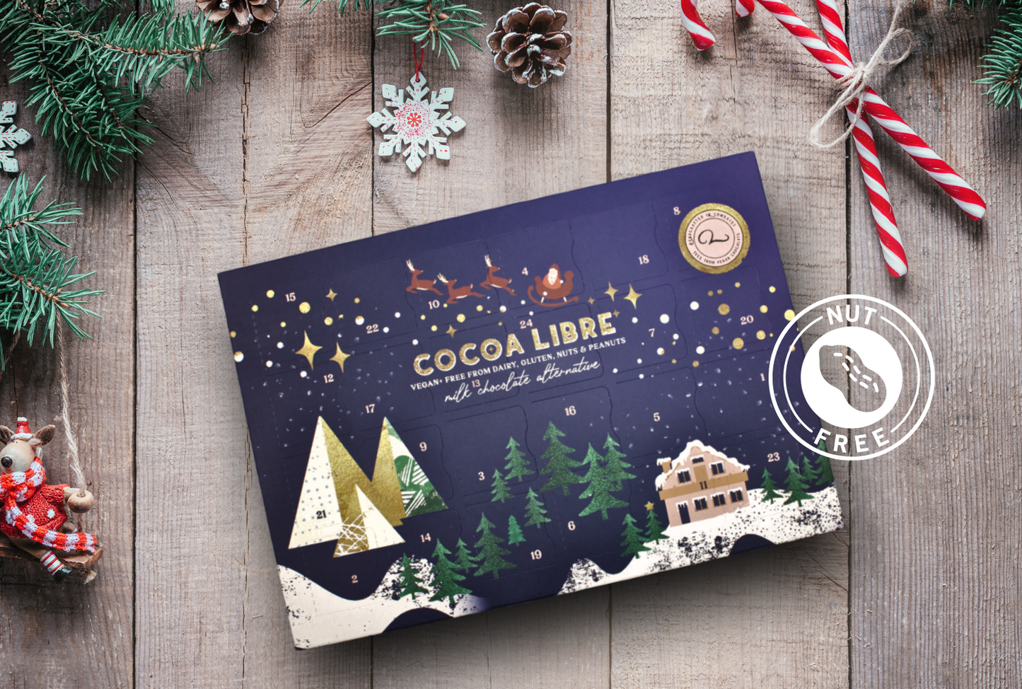 A vegan, dairy free advent calendar for 2023 on a wooden surface with christmas elements around it.